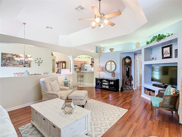 living room with ceiling fan with notable chandelier, a tray ceiling, decorative columns, and dark hardwood / wood-style floors