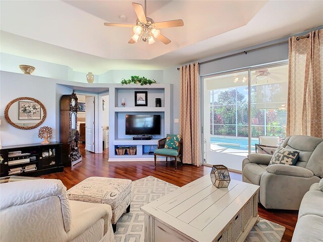 living room with a tray ceiling, ceiling fan, and dark hardwood / wood-style floors