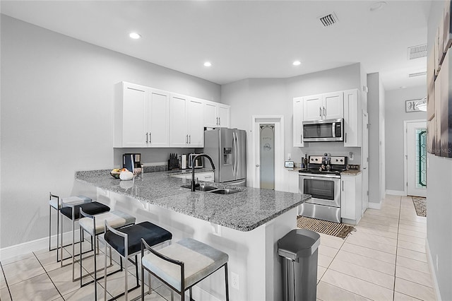 kitchen with appliances with stainless steel finishes, light stone counters, a kitchen bar, and kitchen peninsula