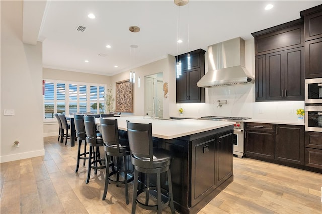 kitchen with a center island with sink, stainless steel appliances, light countertops, wall chimney range hood, and a sink