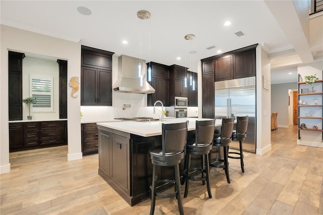 kitchen with built in appliances, light countertops, wall chimney range hood, and light wood-style floors