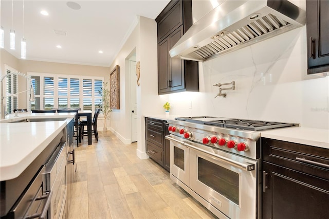 kitchen with range with two ovens, light wood-style flooring, light countertops, crown molding, and wall chimney range hood