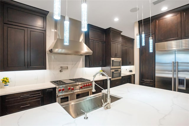 kitchen with dark brown cabinetry, wall chimney exhaust hood, light stone counters, and high end appliances