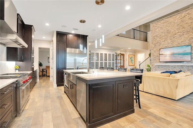 kitchen with light wood-style floors, open floor plan, wall chimney range hood, double oven range, and a sink