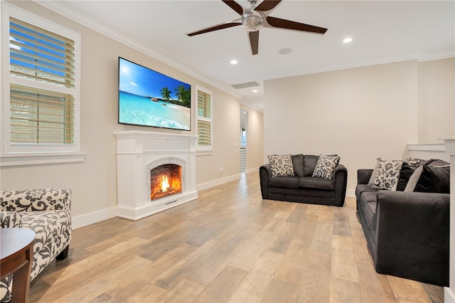 living room featuring light wood finished floors, baseboards, a lit fireplace, crown molding, and recessed lighting