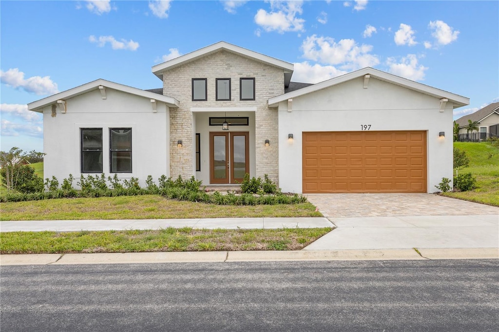 view of front facade featuring a front yard, stucco siding, french doors, decorative driveway, and an attached garage