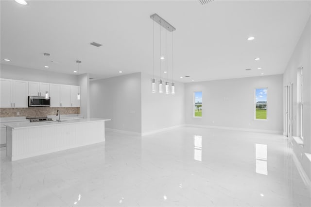 kitchen with an island with sink, stainless steel appliances, backsplash, pendant lighting, and white cabinetry