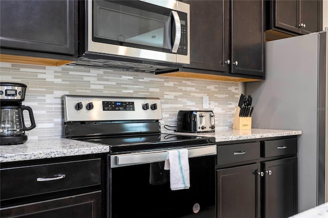 kitchen featuring dark brown cabinetry, decorative backsplash, stainless steel appliances, and light stone countertops