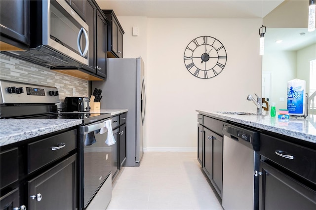 kitchen featuring tasteful backsplash, baseboards, light stone countertops, stainless steel appliances, and a sink