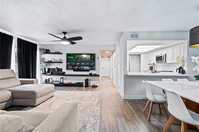 living room with a textured ceiling, wood-type flooring, and ceiling fan