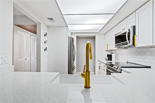 kitchen featuring white cabinets, appliances with stainless steel finishes, backsplash, and light stone countertops