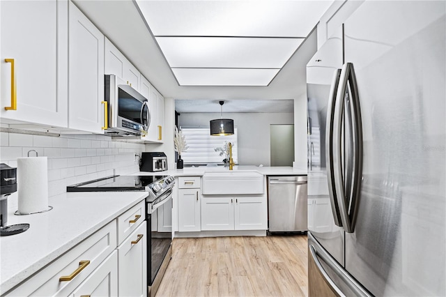 kitchen with white cabinets, decorative light fixtures, stainless steel appliances, light hardwood / wood-style floors, and sink