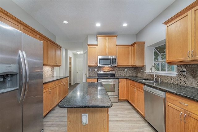 kitchen with a kitchen island, sink, dark stone counters, stainless steel appliances, and light hardwood / wood-style flooring