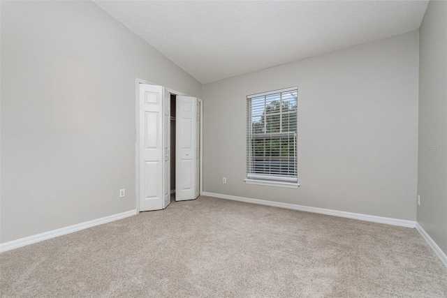 unfurnished bedroom featuring lofted ceiling, light colored carpet, and a textured ceiling