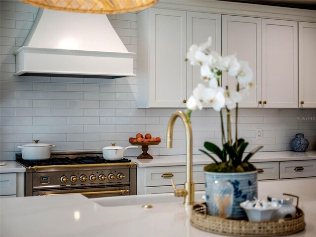 kitchen with backsplash, stainless steel stove, custom range hood, and white cabinets