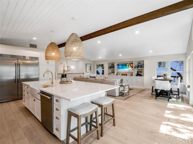 kitchen with appliances with stainless steel finishes, decorative light fixtures, white cabinetry, an island with sink, and light wood-type flooring