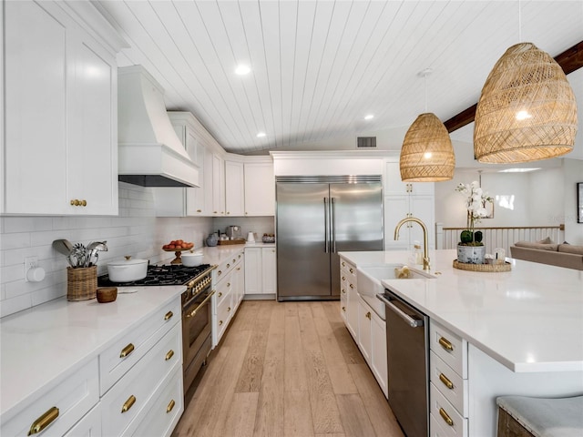 kitchen with premium range hood, sink, white cabinetry, premium appliances, and pendant lighting