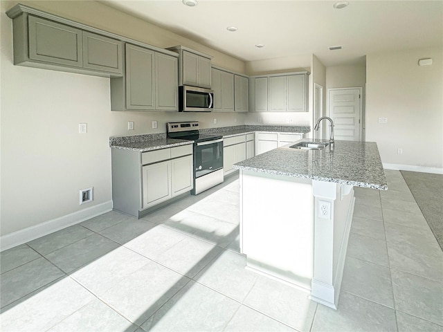 kitchen with light stone counters, light tile patterned flooring, sink, a center island with sink, and appliances with stainless steel finishes