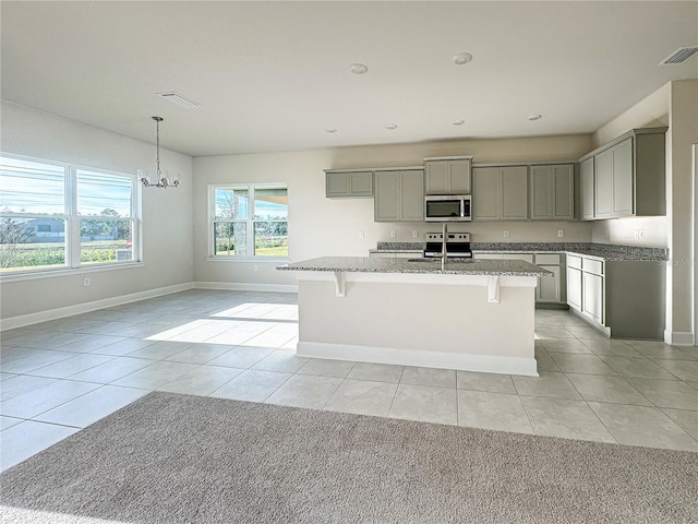 kitchen with light stone counters, light tile patterned flooring, a center island with sink, gray cabinets, and stainless steel appliances