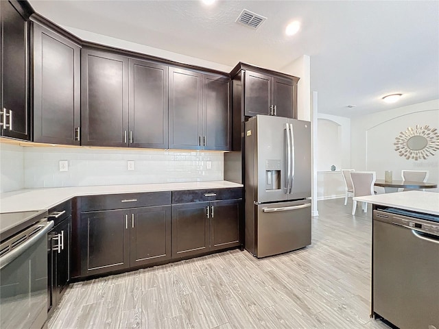 kitchen featuring light wood-type flooring, appliances with stainless steel finishes, decorative backsplash, and dark brown cabinetry