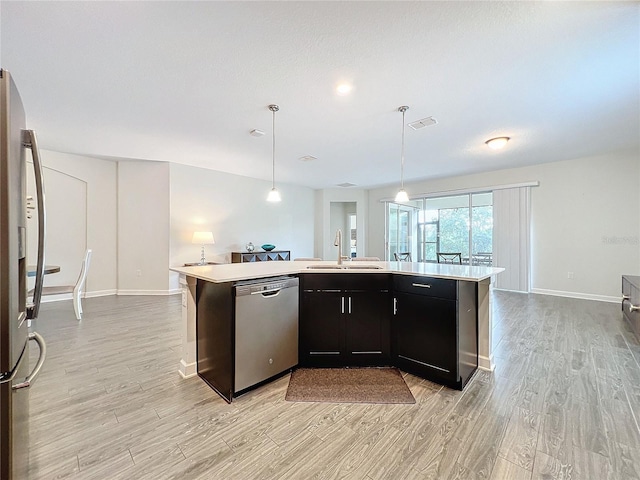 kitchen with appliances with stainless steel finishes, hanging light fixtures, a kitchen island with sink, and sink