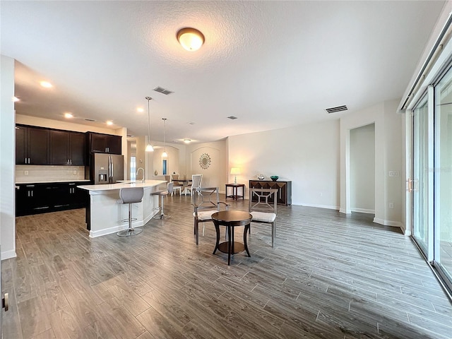 kitchen featuring a kitchen breakfast bar, pendant lighting, wood-type flooring, stainless steel fridge with ice dispenser, and a kitchen island with sink