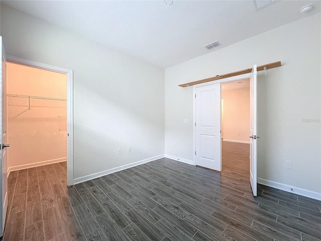 unfurnished bedroom with a closet, a spacious closet, a barn door, and dark hardwood / wood-style floors