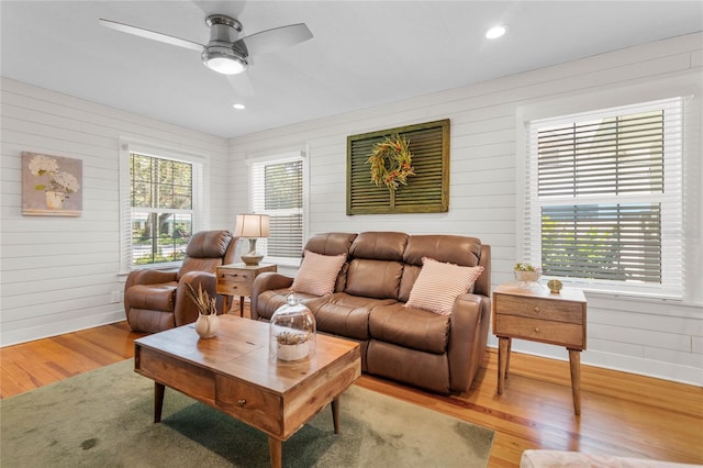 living room with light wood-type flooring, wooden walls, ceiling fan, and a healthy amount of sunlight