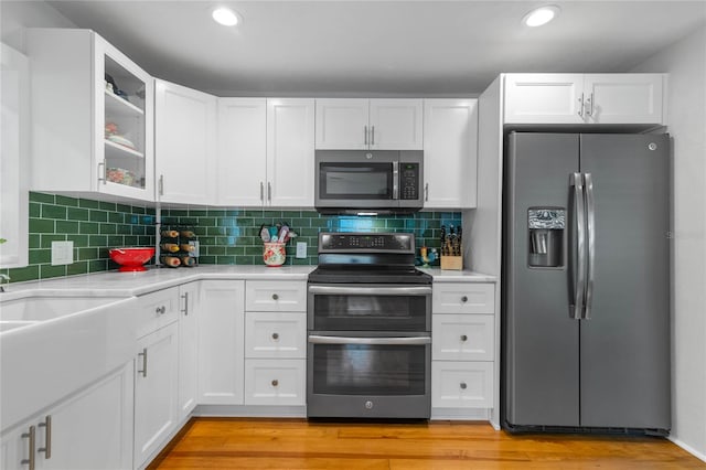 kitchen with decorative backsplash, white cabinets, stainless steel appliances, and light wood-type flooring