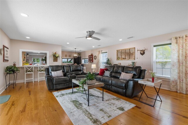 living room featuring a textured ceiling, ceiling fan with notable chandelier, and light hardwood / wood-style flooring