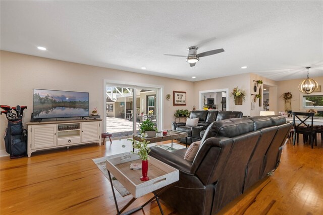 living room with ceiling fan with notable chandelier, a textured ceiling, and light hardwood / wood-style flooring