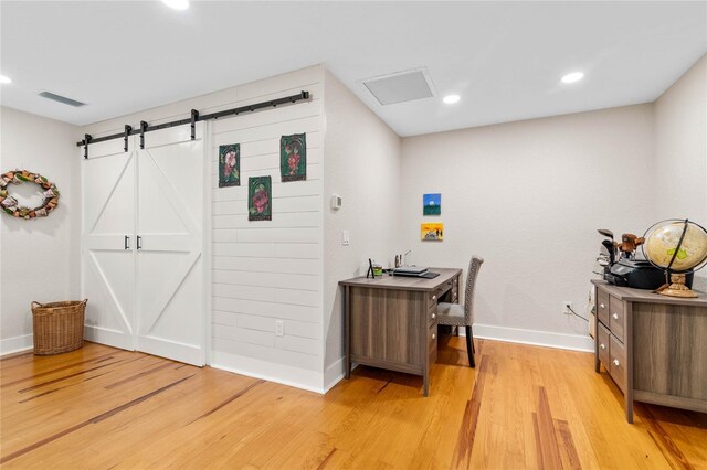 office with a barn door and light hardwood / wood-style flooring