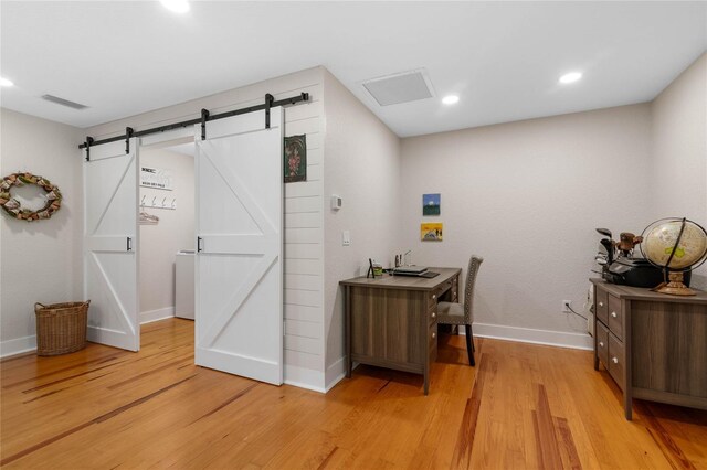 home office with a barn door and light hardwood / wood-style flooring