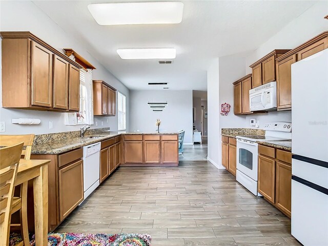 kitchen featuring white appliances, light stone counters, kitchen peninsula, and sink