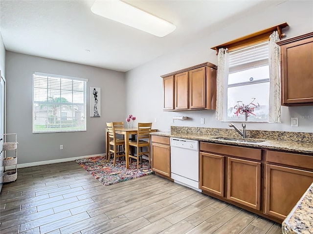 kitchen with dishwasher, sink, light stone countertops, and light hardwood / wood-style floors