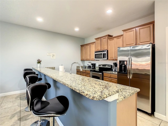 kitchen with a kitchen breakfast bar, light stone countertops, light tile patterned floors, stainless steel appliances, and sink