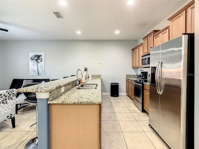 kitchen with light stone countertops, stainless steel appliances, sink, kitchen peninsula, and a breakfast bar area