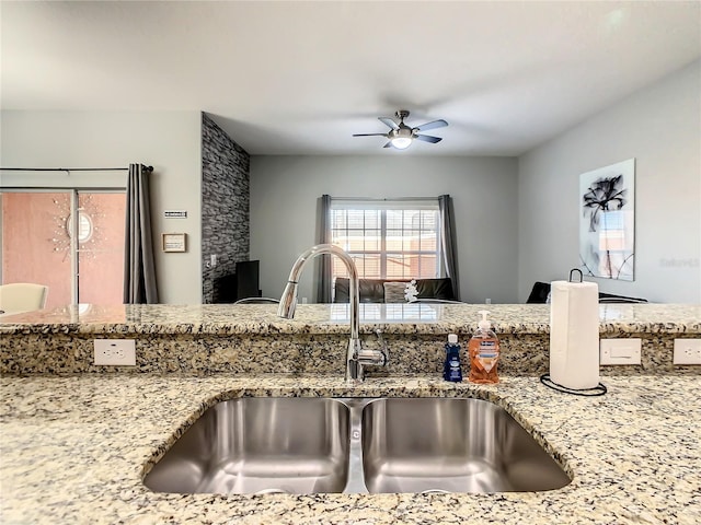 kitchen with light stone counters, ceiling fan, and sink