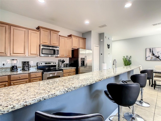 kitchen featuring light tile patterned floors, a breakfast bar area, light stone counters, and stainless steel appliances