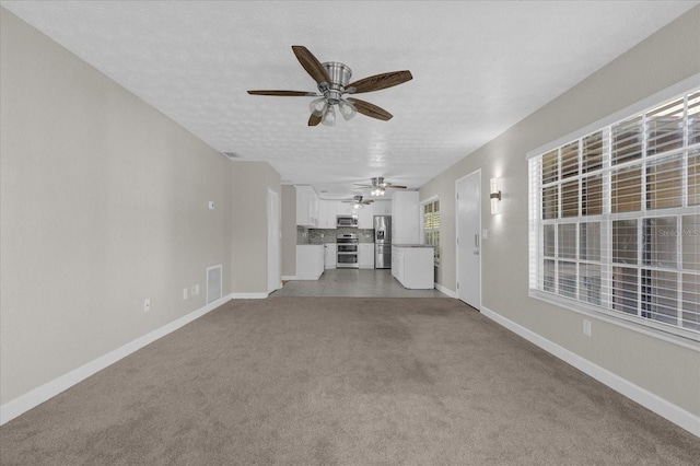 unfurnished living room with light colored carpet, ceiling fan, and a textured ceiling