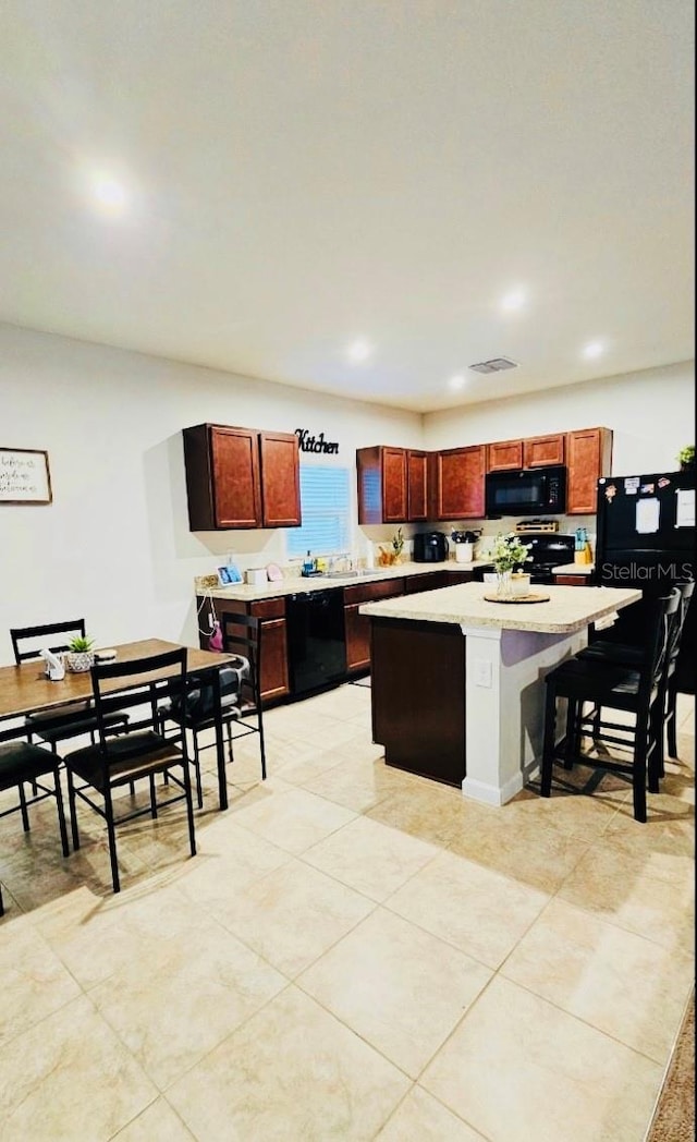 kitchen featuring black appliances, a kitchen island, light tile patterned floors, and a breakfast bar