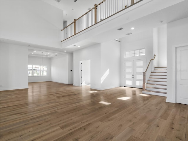 unfurnished living room featuring a high ceiling, hardwood / wood-style flooring, and french doors