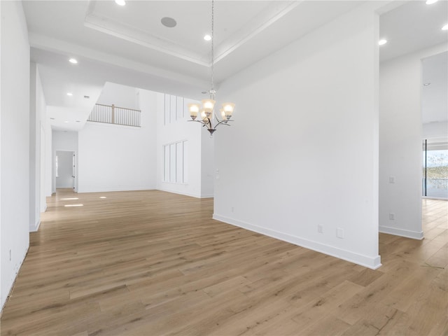 empty room featuring a raised ceiling, light hardwood / wood-style flooring, and a notable chandelier