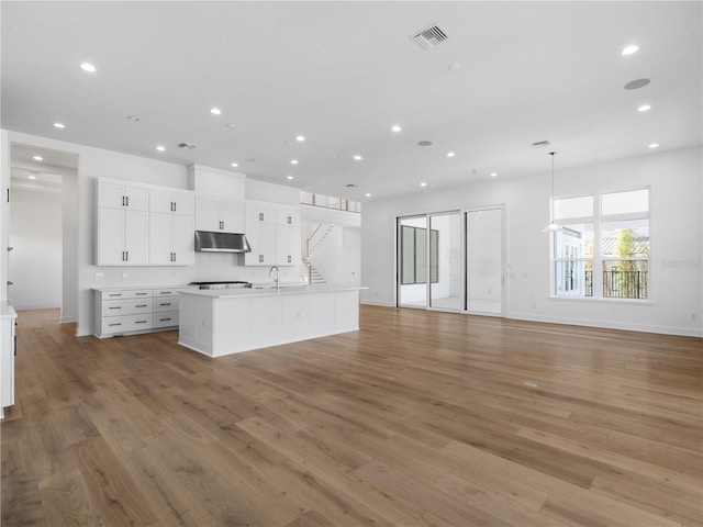 kitchen with a center island with sink, white cabinets, wood-type flooring, and decorative light fixtures