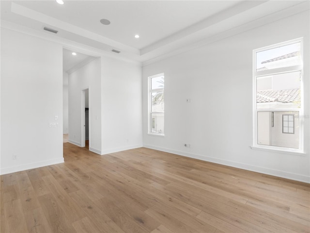 spare room with a raised ceiling, crown molding, and light hardwood / wood-style floors