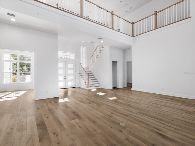 unfurnished living room featuring wood-type flooring, a towering ceiling, and french doors