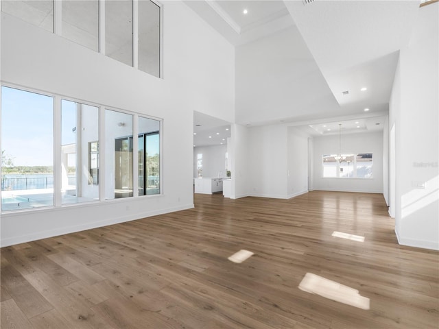 unfurnished living room featuring hardwood / wood-style flooring, a healthy amount of sunlight, a high ceiling, and an inviting chandelier