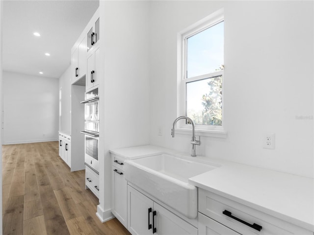 kitchen with light wood-type flooring, white cabinetry, double oven, and sink