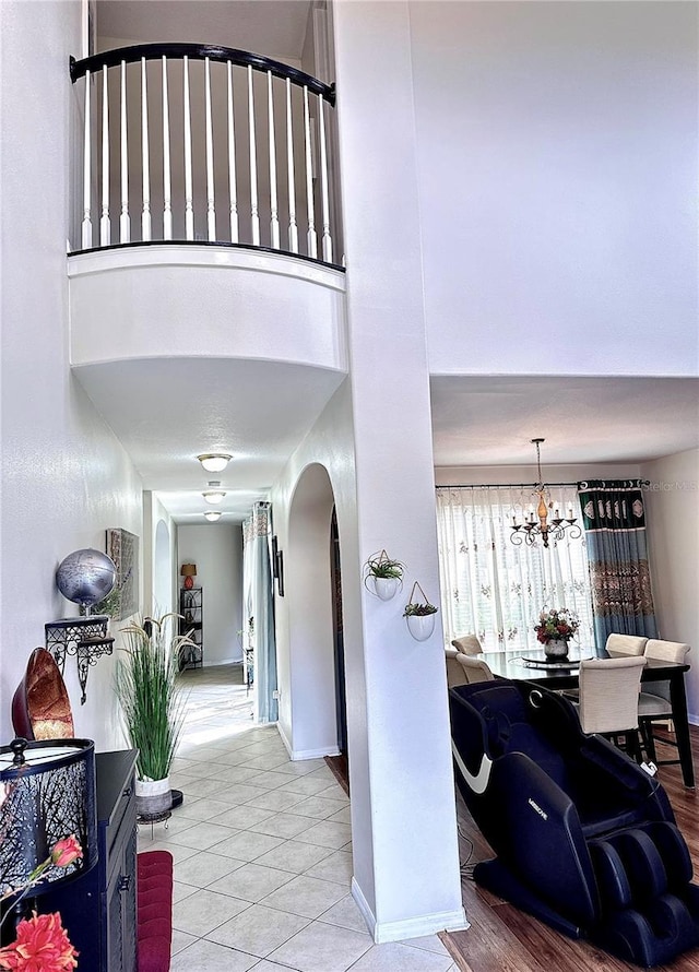 interior space featuring arched walkways, tile patterned flooring, baseboards, a notable chandelier, and a high ceiling