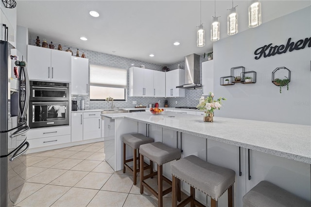 kitchen featuring a breakfast bar area, backsplash, light tile patterned floors, stainless steel appliances, and wall chimney exhaust hood
